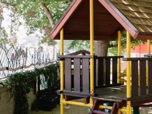 A playground platform with a shingled roof and burgundy ladder in front of a tree with lots of foliage.