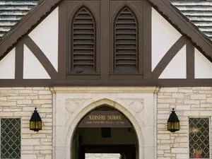 A flat stone building with a center stone arch. A sign hangs from the arch and says: Nursery School.